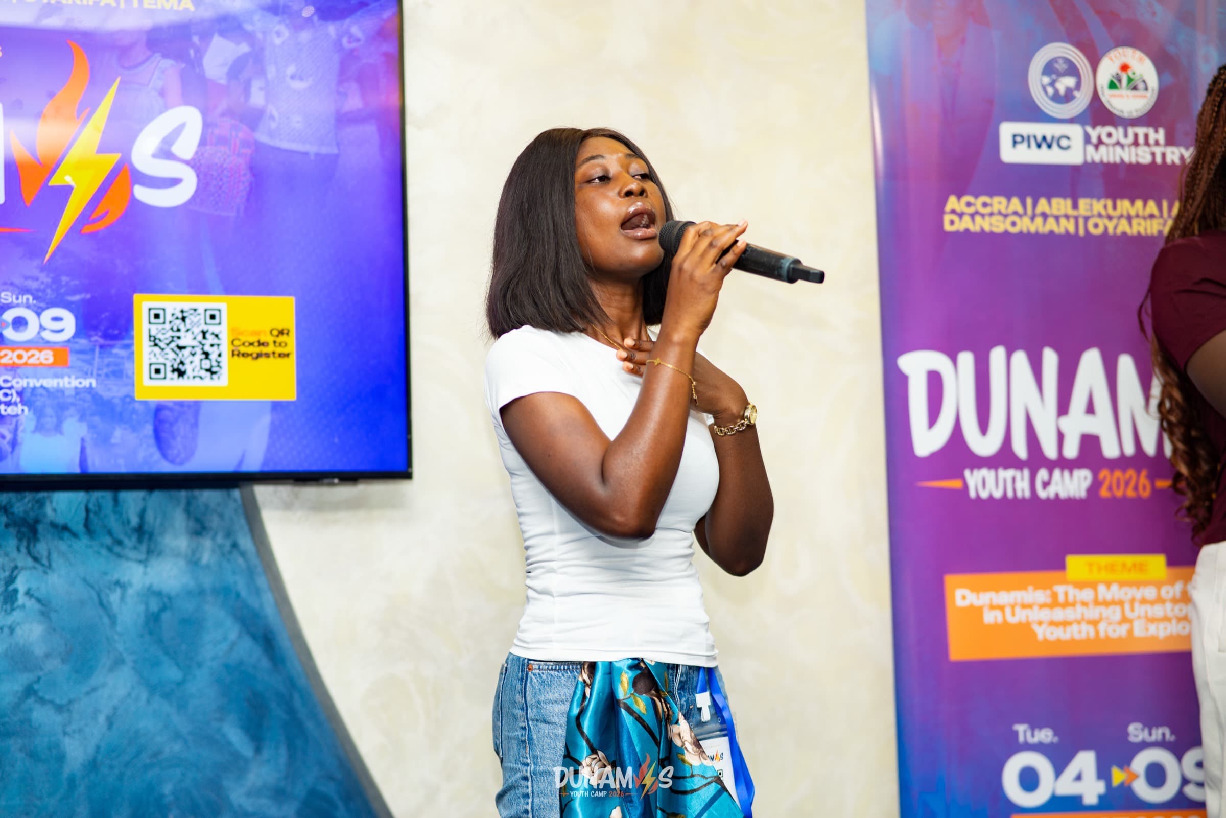 A camper leading worship on stage in front of the Dunamis Youth Camp 2026 banner